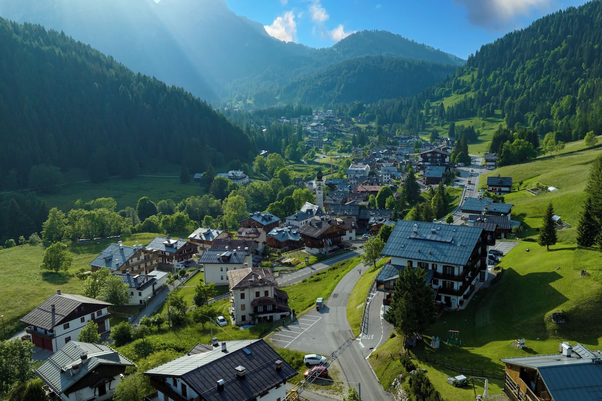 A small town with a central street, surrounded by green hills and mountains.