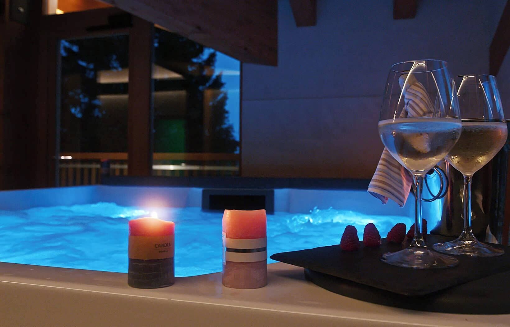 Un bain à remous avec des bougies et des verres disposés sur une table, créant une ambiance propice à une soirée relaxante.