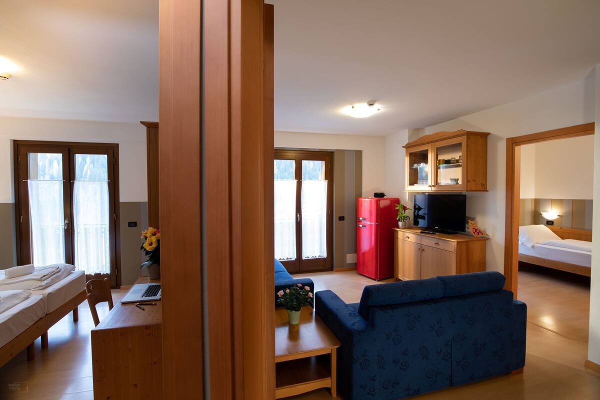 A compact living space with a bed, a desk with a laptop, a blue sofa, a red refrigerator, and a wooden cabinet.