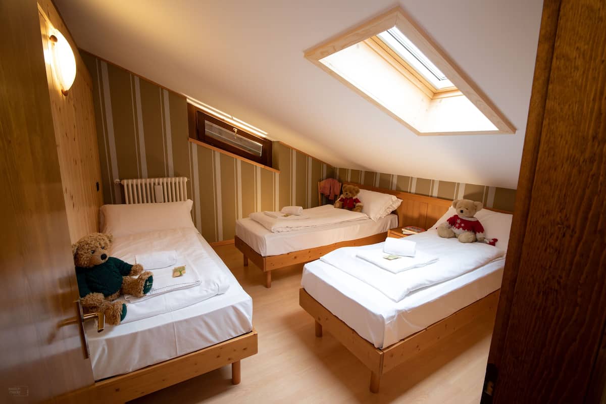 A cozy attic bedroom with two wooden beds, a skylight, and a teddy bear on one bed.