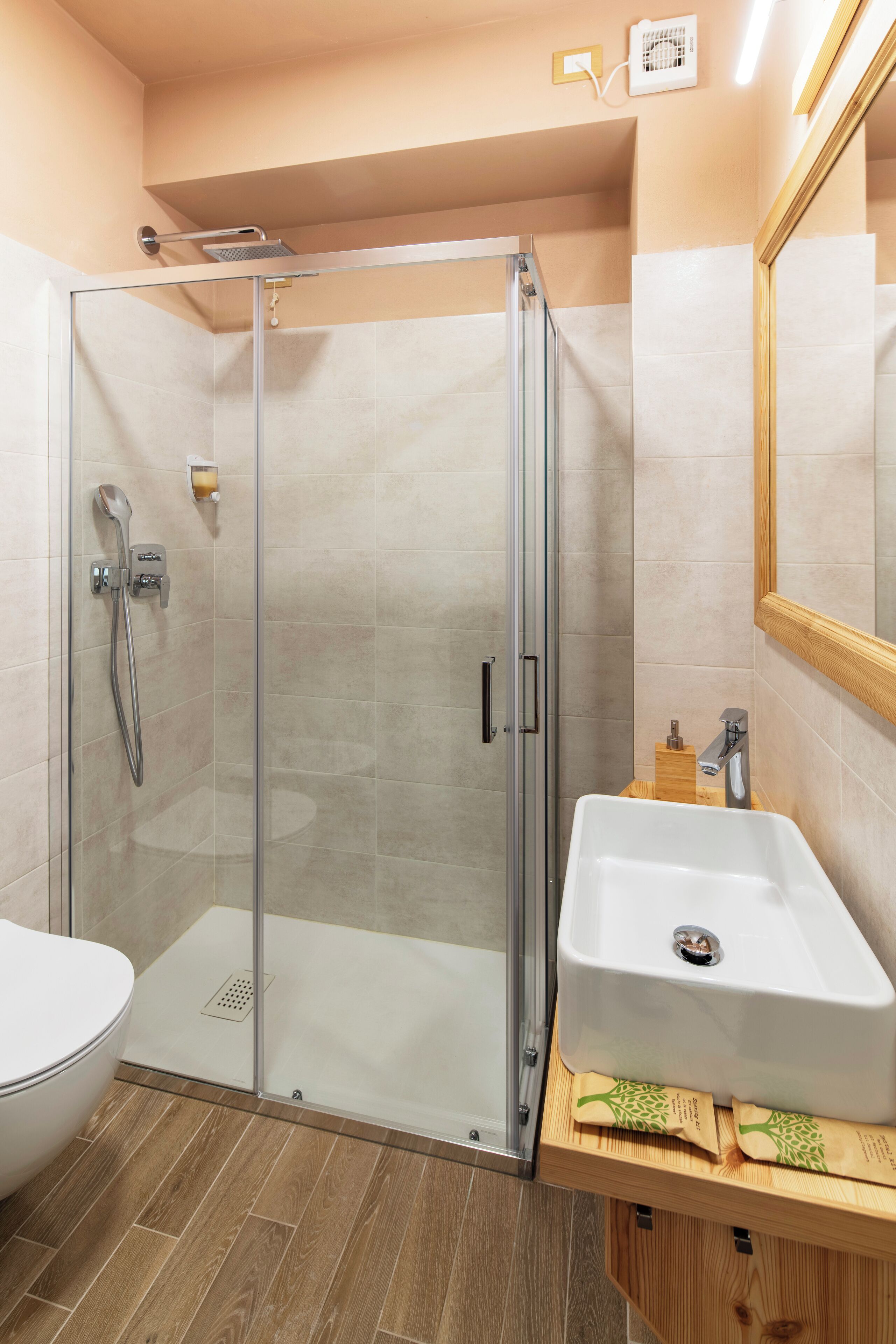 A modern bathroom with a glass-enclosed shower, a white sink, and a wooden vanity.