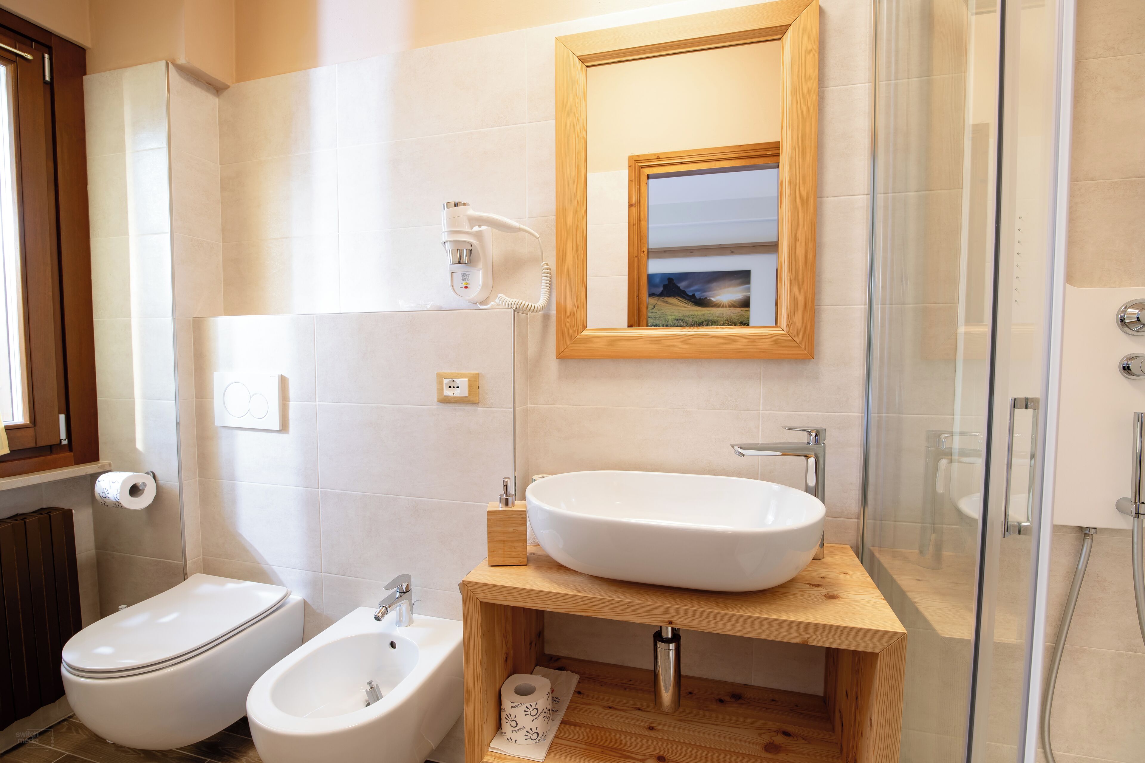 Un baño moderno con inodoro, bidé y un lavamanos grande con tocador de madera.