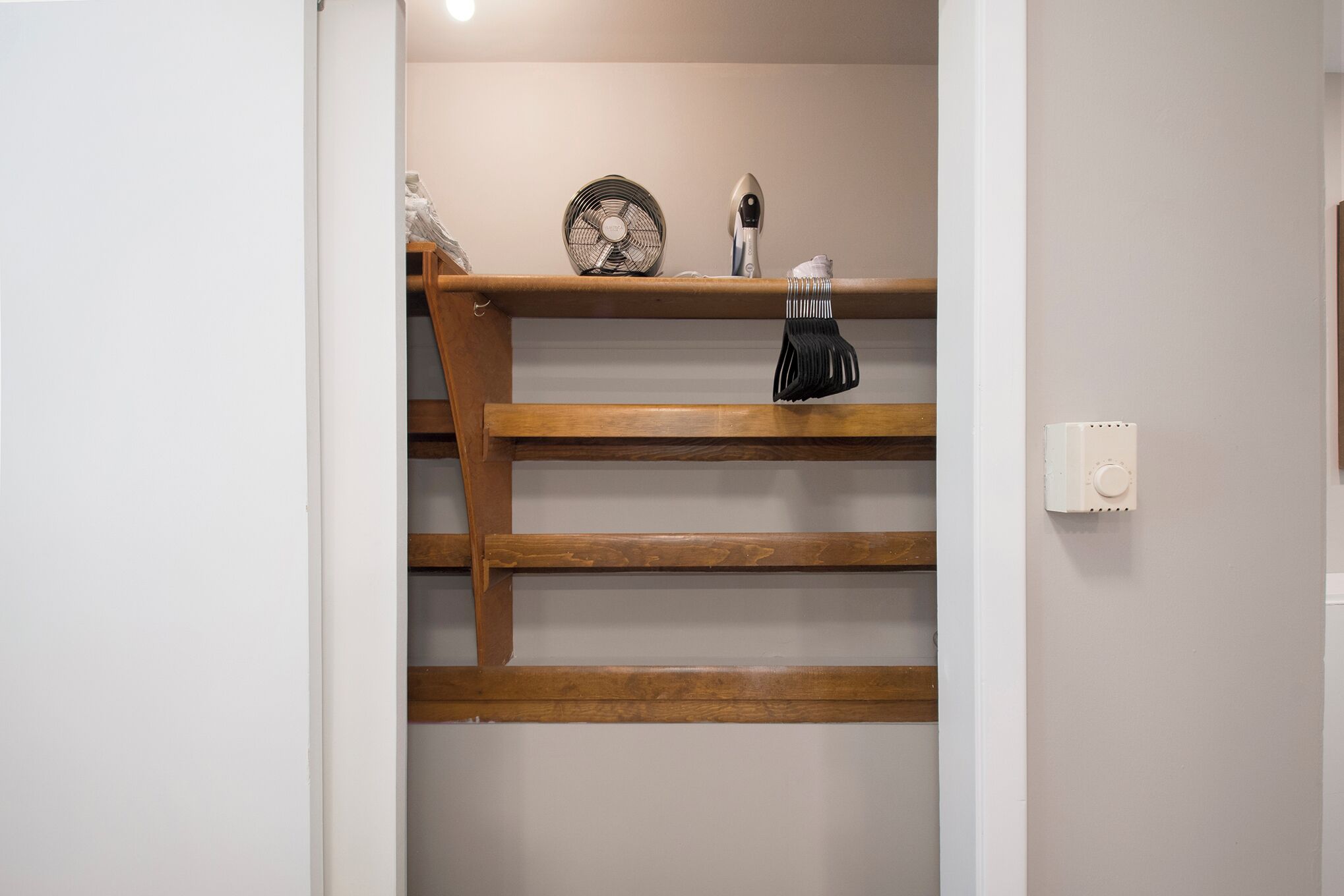 A wooden shelf with a fan, a hairdryer, and a white object.