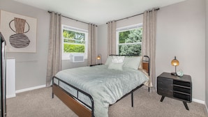 A bedroom with a bed, bedside tables, a wall-mounted lamp, and a window with curtains.