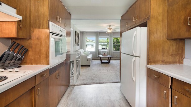 A kitchen with wooden cabinets, a white countertop, and a dining area with a table and chairs.