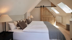Une chambre à coucher avec un lit, deux lampes de chevet, une porte en bois et des fenêtres de toit.
