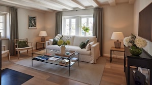 Un salon moderne avec un canapé blanc, une table basse en verre et un plancher en bois. On y trouve deux tables d’appoint avec des lampes et un vase rempli de fleurs.