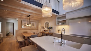 Une cuisine moderne dotée d’un grand îlot central, d’un plafond en bois, de luminaires suspendus et offrant une vue sur l’espace repas.