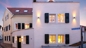 Un immeuble de deux étages avec une façade blanche, des volets noirs et une plaque de rue bleue indiquant « Weinbergstraße ».