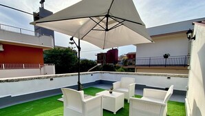 Una terrazza sul tetto con prato sintetico verde, mobili in vimini bianco e un ombrellone che offre ombra.