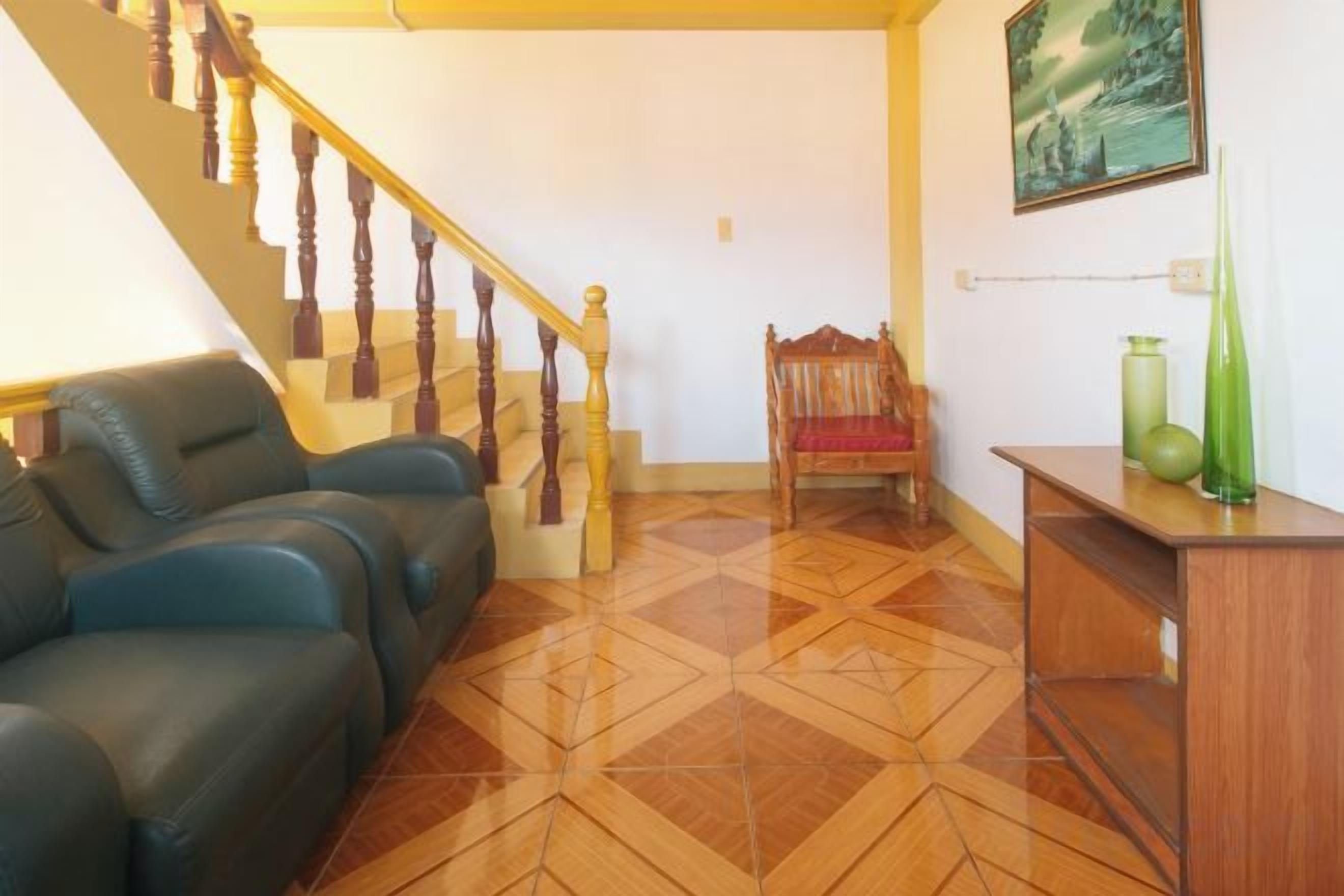 Una sala de estar con una escalera, un sofá, una silla y un aparador de madera.