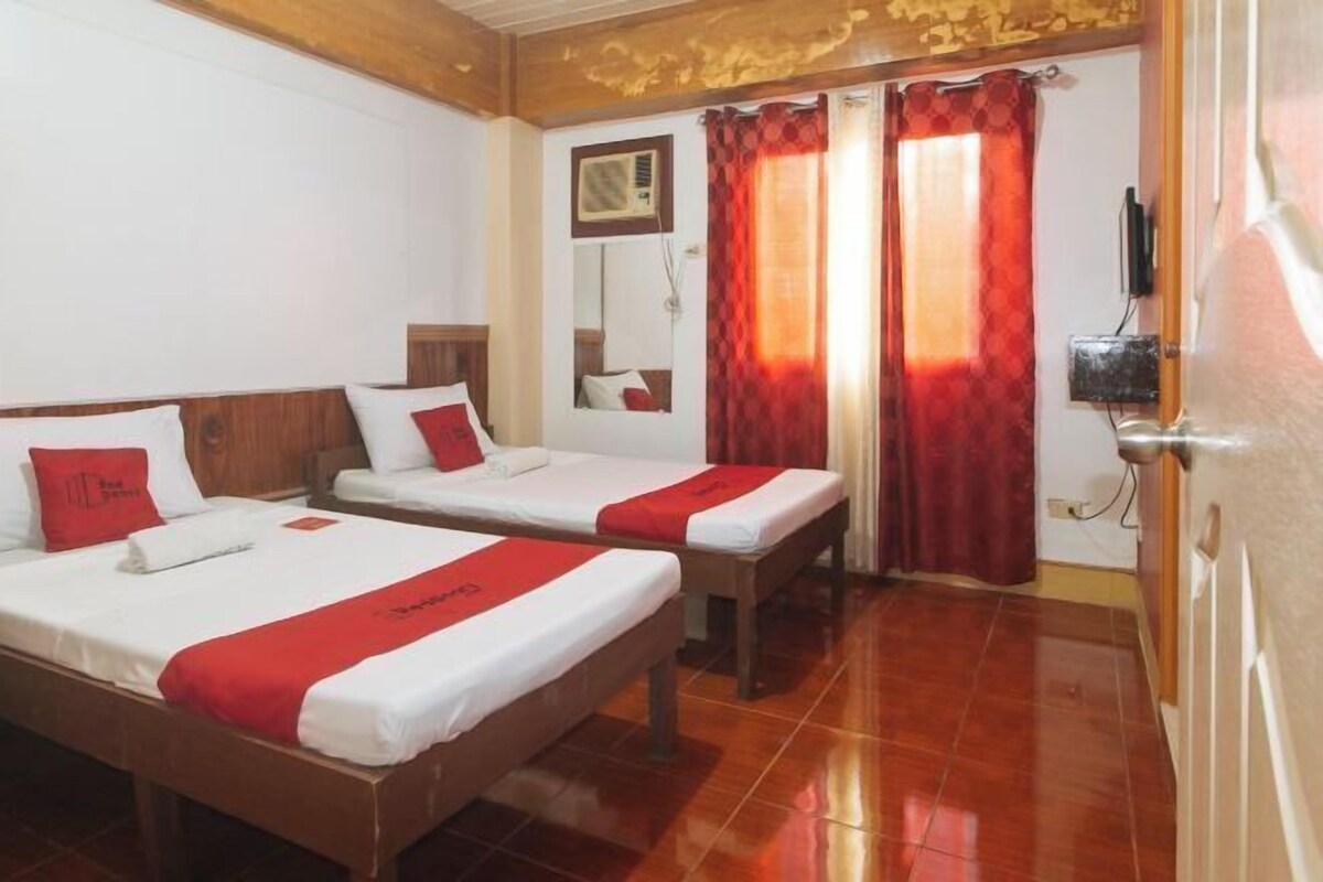 A hotel room with two beds, each with red and white bedding, a wooden headboard, a small bedside table, and a mirror on the wall.