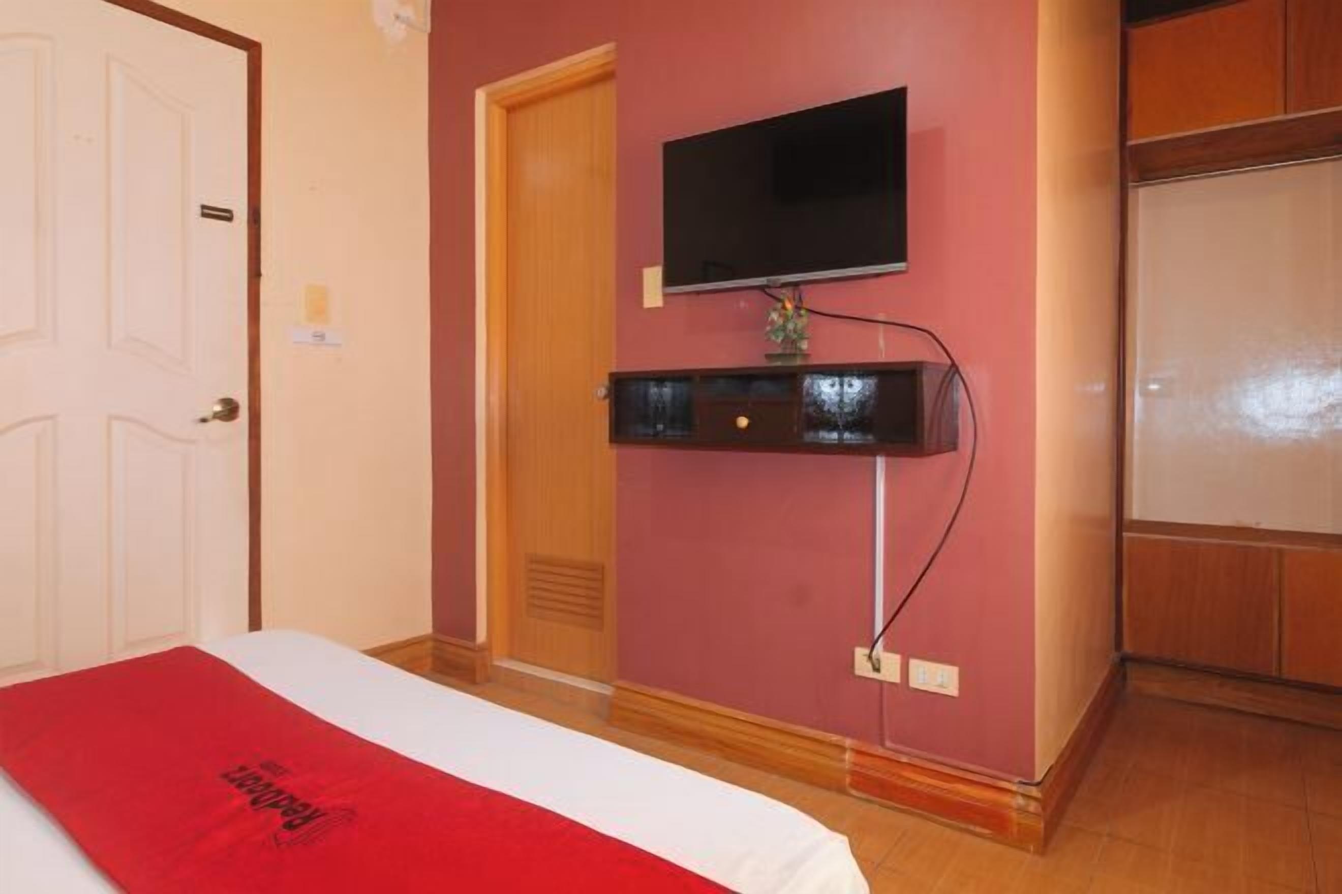 Una habitación de hotel con una cama, un televisor montado y una puerta de madera.