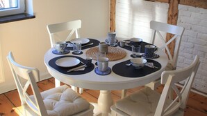 A round dining table with white chairs, blue and white plates, and a hanging pendant light. - Mobys Hafenglück - Gemütliche 3-zimmer-wohnung für Groß und Klein (Neustadt in Holstein)
