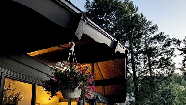 Una terraza moderna al aire libre con asientos, una maceta colgante y vistas al interior.