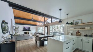 Una cocina moderna con armarios blancos, una isla grande y un comedor con techo de madera.