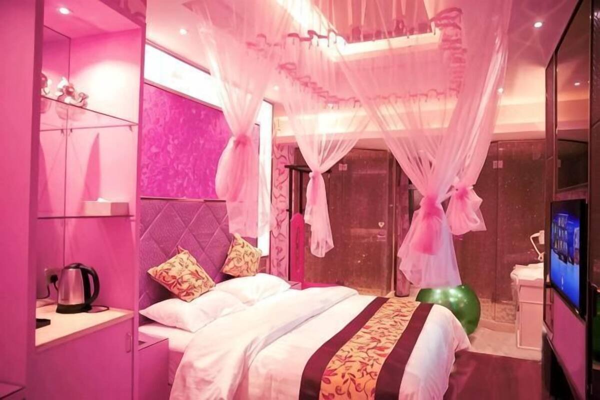 Une chambre à coucher comprenant un lit, un téléviseur, un objet de décoration vert et un miroir.
