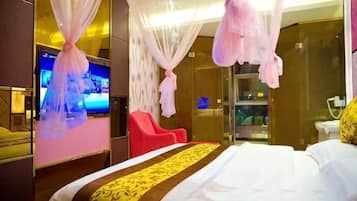 A hotel room with a bed, a TV, a red chair, and a glass shower area.
