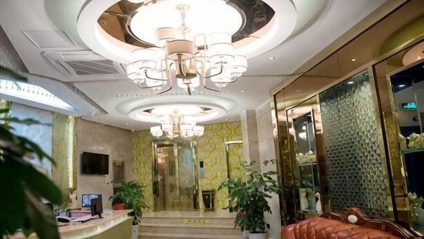 Eine Hotelhalle mit einer Rezeption, einem Ledersofa, einem Chandelier und einer Treppe zu den oberen Etagen.