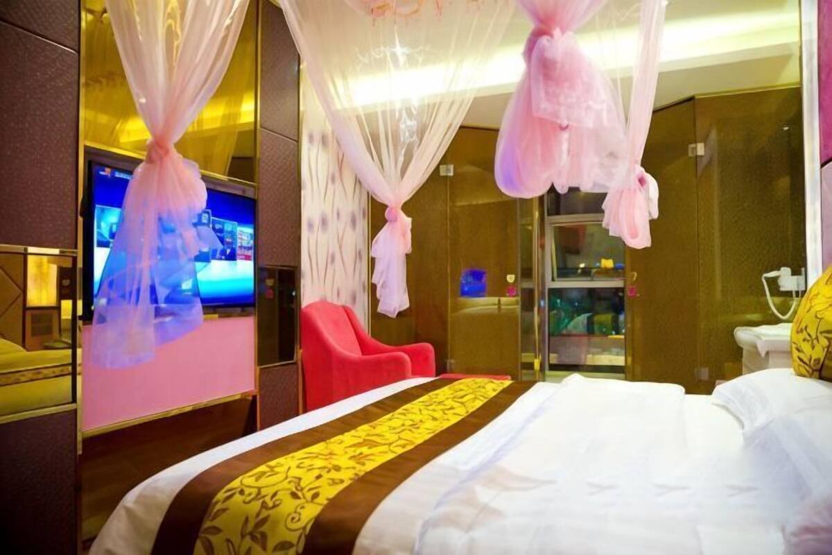 Une chambre d’hôtel avec un lit, un fauteuil rouge, une télévision et une douche en verre.