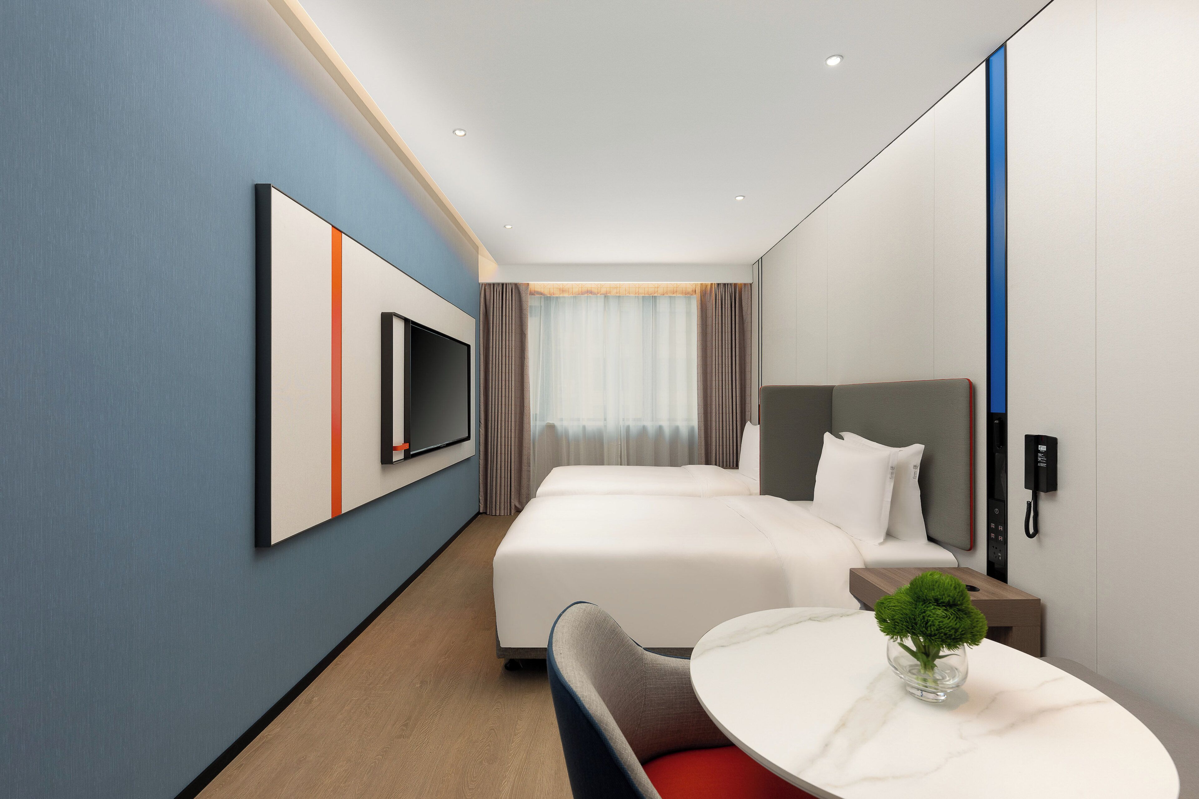 A modern hotel room with a large bed, a desk with a chair, a flat-screen TV mounted on the wall, and a telephone.