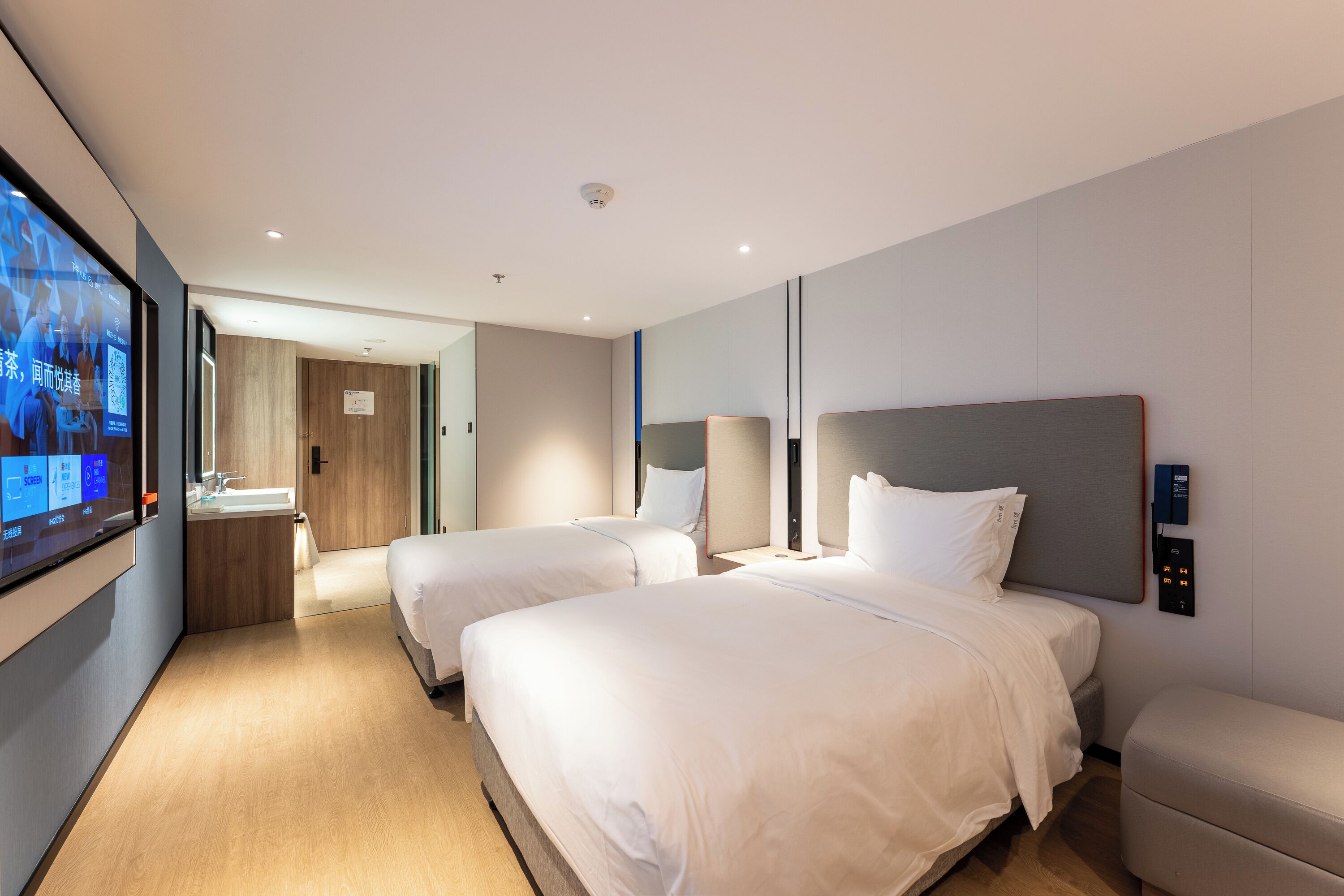 Habitación de hotel con dos camas, televisión, mesita de noche y baño con lavabo y espejo.
