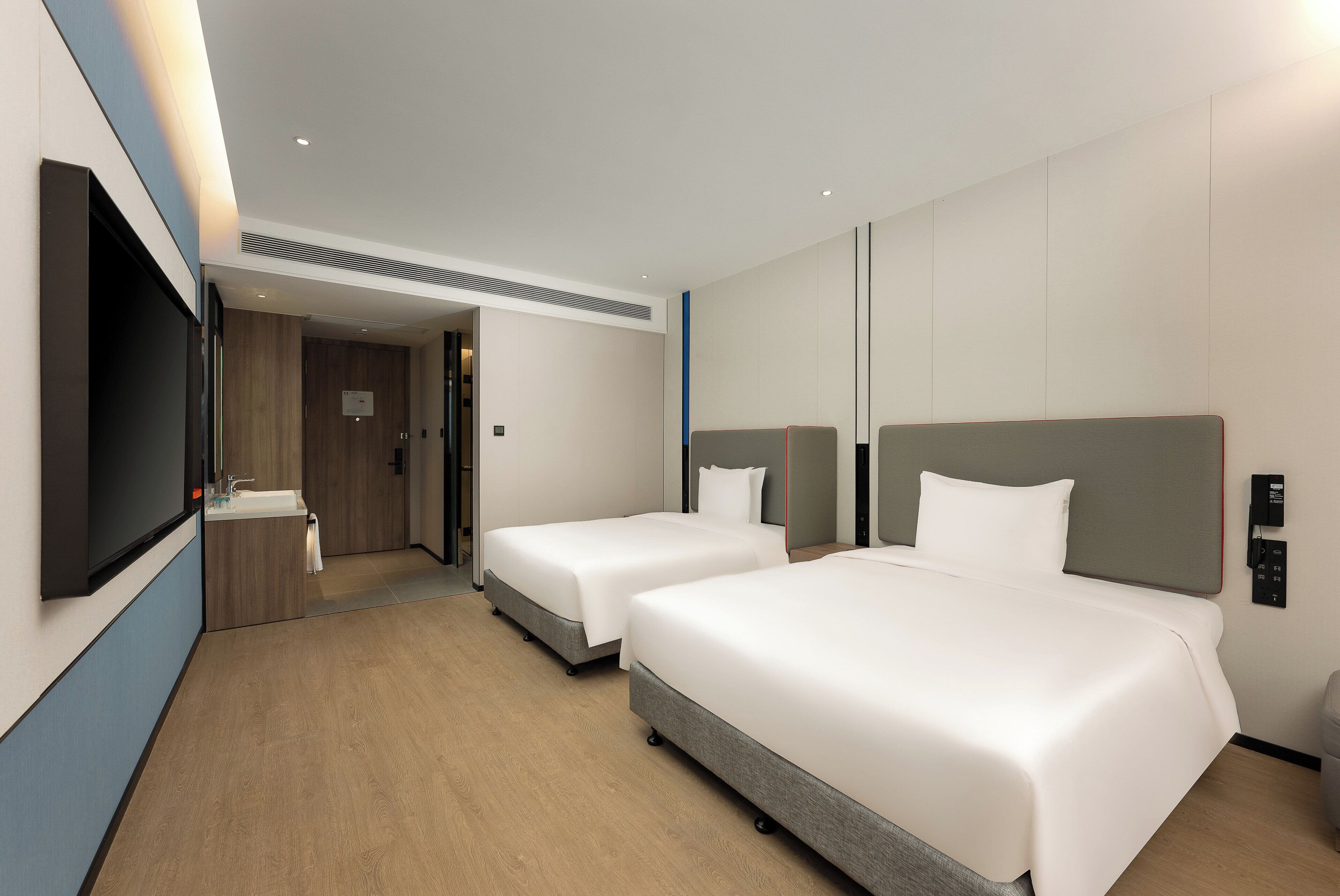 A hotel room with two beds, a TV, a sink, and a mirror.