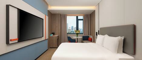 A modern hotel room with a large bed, a TV, a desk, and a view of the city.