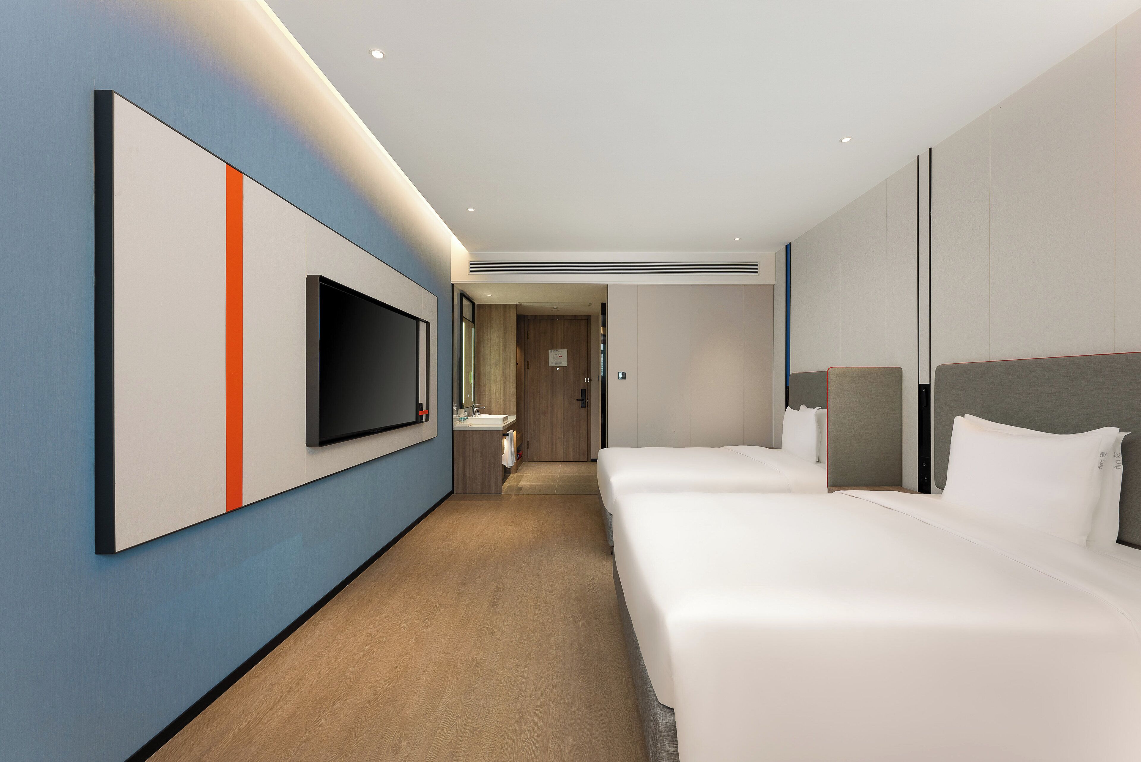 A modern hotel room with a large bed, a TV mounted on the wall, and a wooden floor.