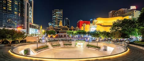 A modern urban plaza with a circular amphitheater, surrounded by contemporary buildings and trees.