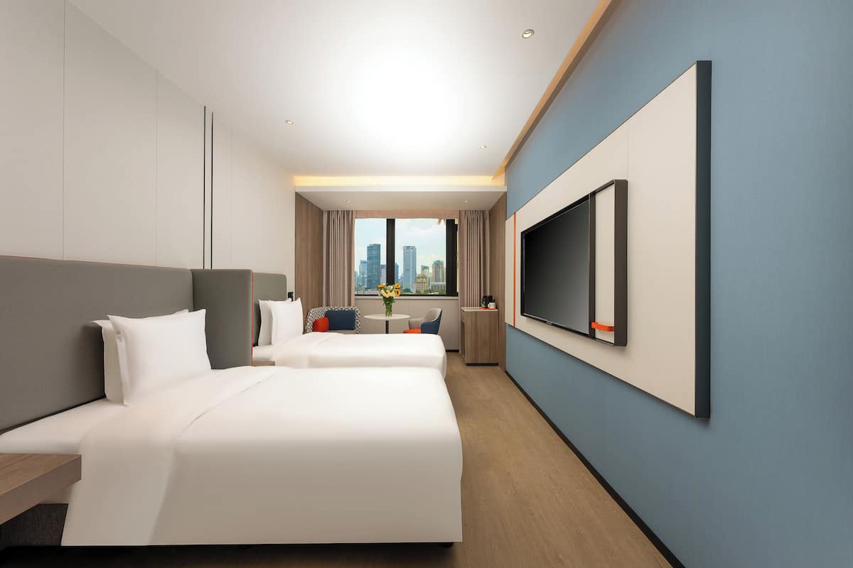 A modern hotel room with two beds, a large TV, and a city view.
