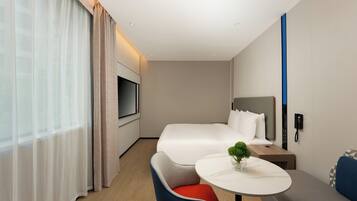 Una habitación de hotel moderna con cama, televisión, mesita de noche con una planta, una silla y una pequeña mesa.