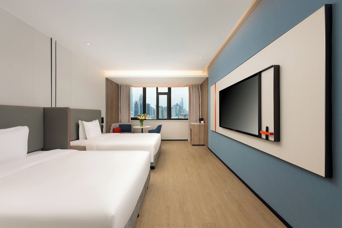 Una habitación de hotel moderna con dos camas, un televisor, un escritorio y vistas a la ciudad.