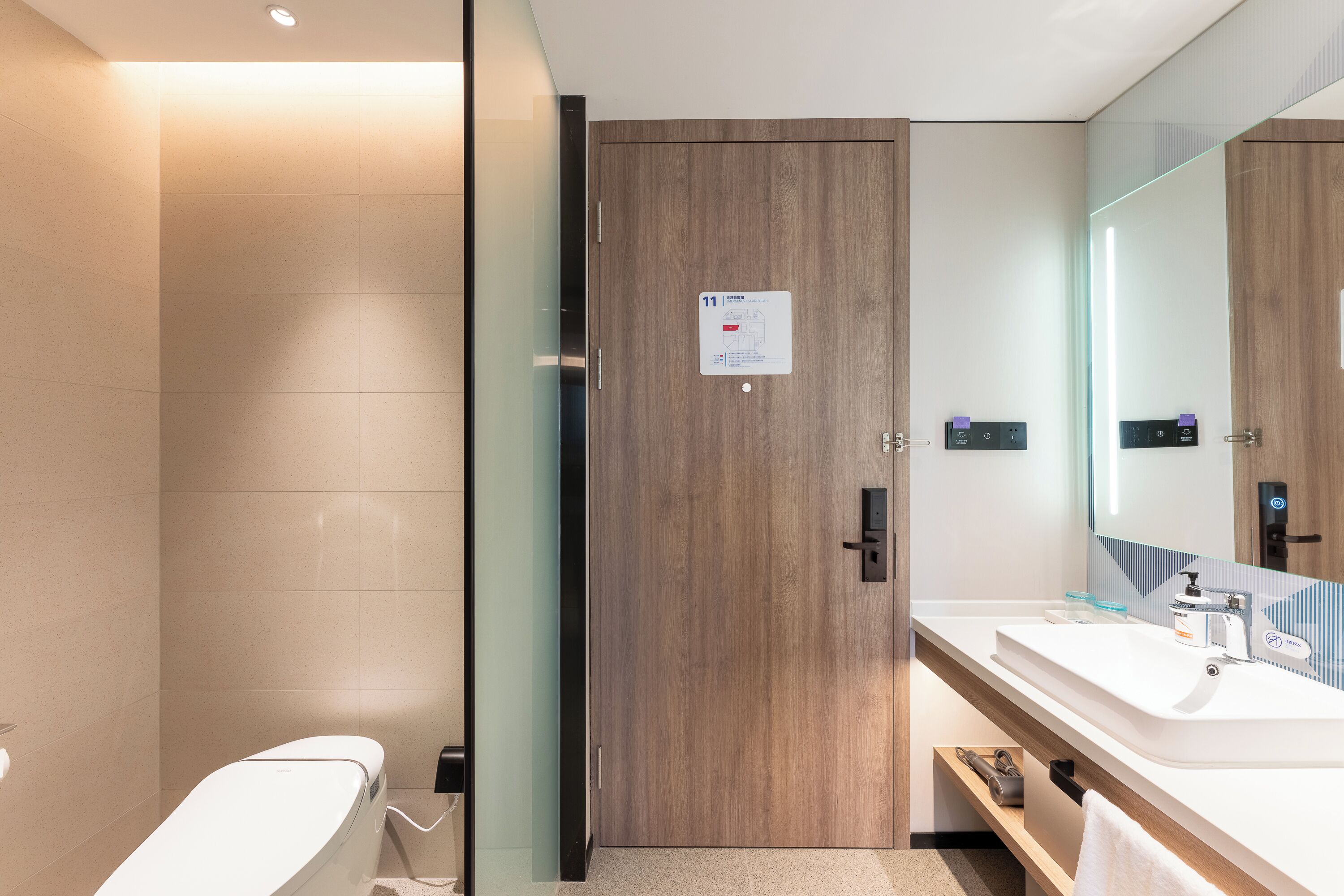 Un bagno moderno con una porta in legno, cabina doccia in vetro, lavabo bianco e uno specchio grande.
