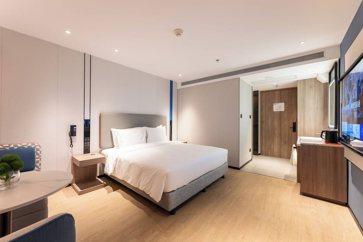 A modern hotel room with a large bed, bedside tables, a desk, and a TV.