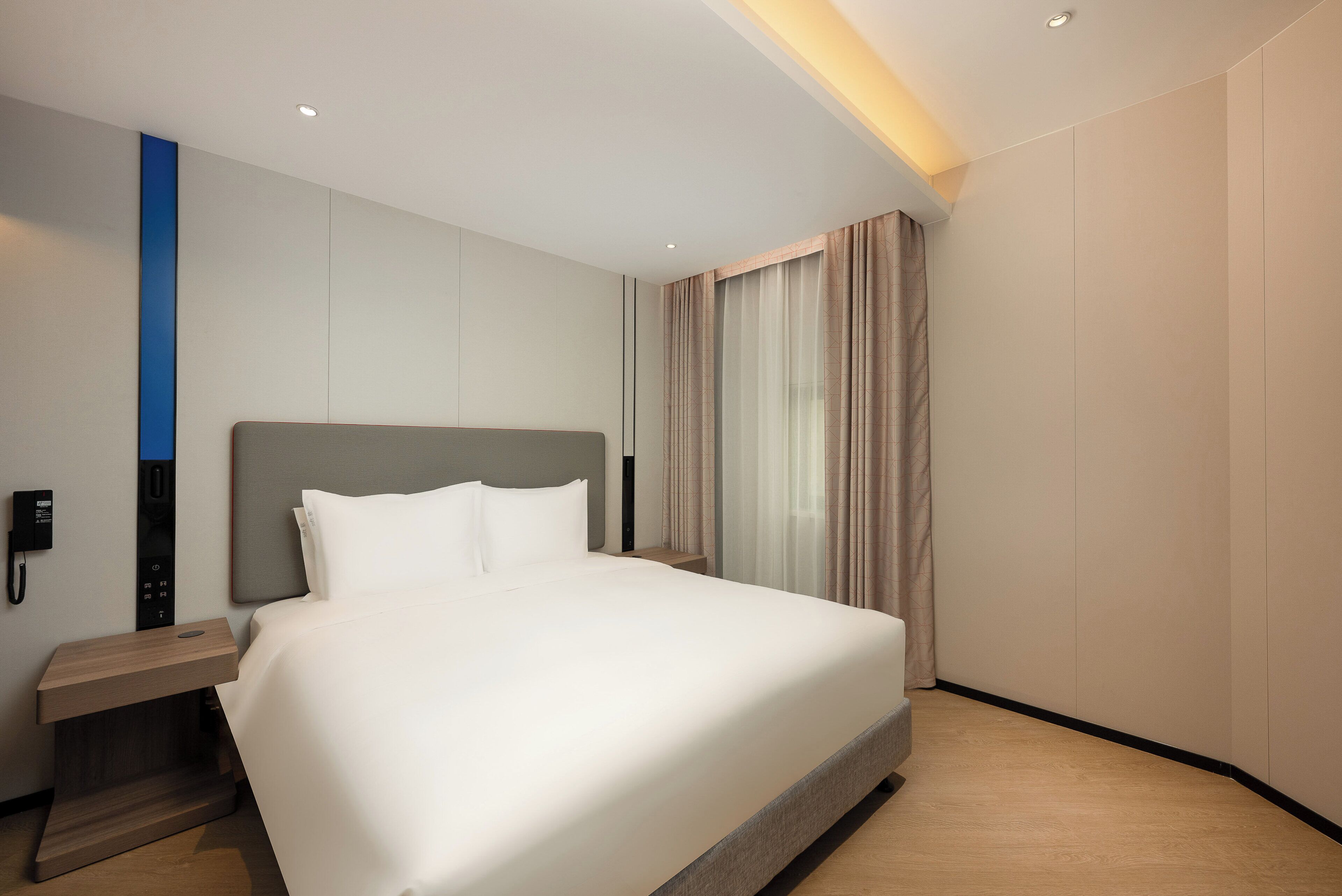 Une chambre d’hôtel moderne, dotée d’un grand lit, d’une table de chevet avec un téléphone et d’un panneau de commande fixé au mur.
