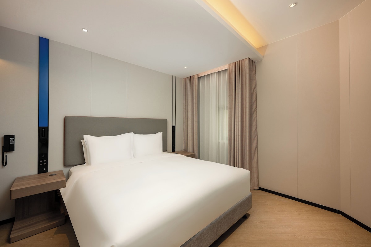 Una habitación de hotel moderna con una cama grande, una mesita de noche con teléfono y un panel de control en la pared.