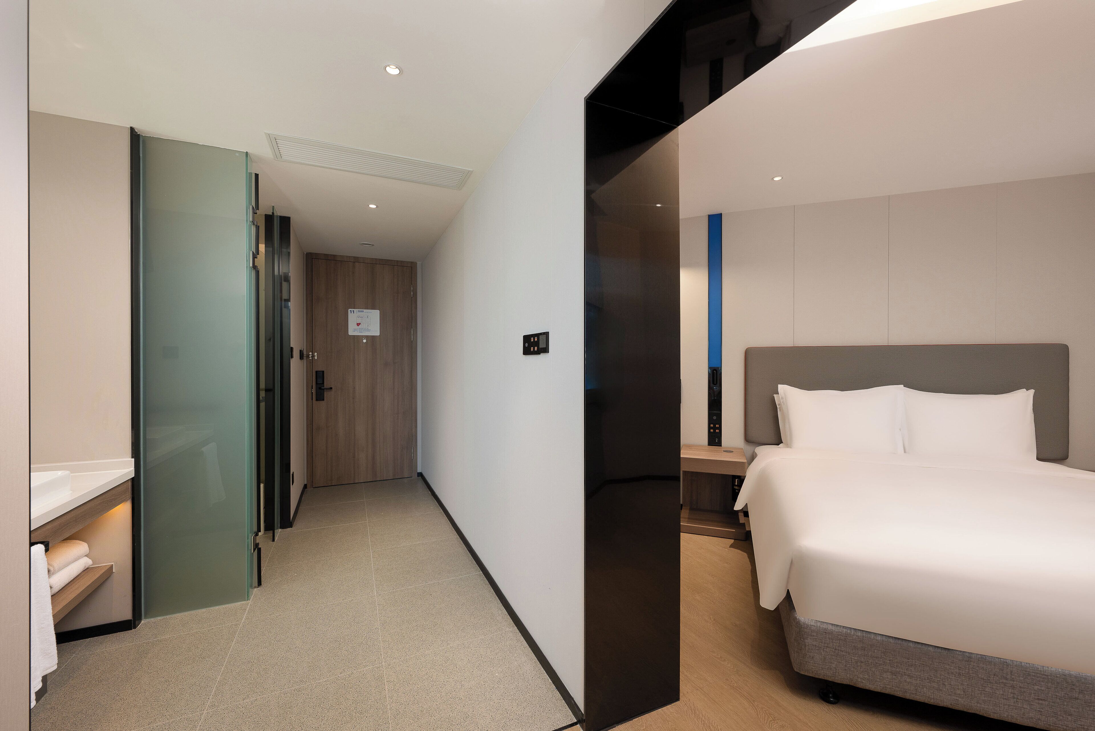 A modern hotel room with a large bed, a bedside table, and a glass partition wall.