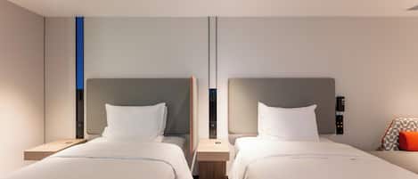 A modern hotel room with two beds, a small table, and a wall-mounted phone.