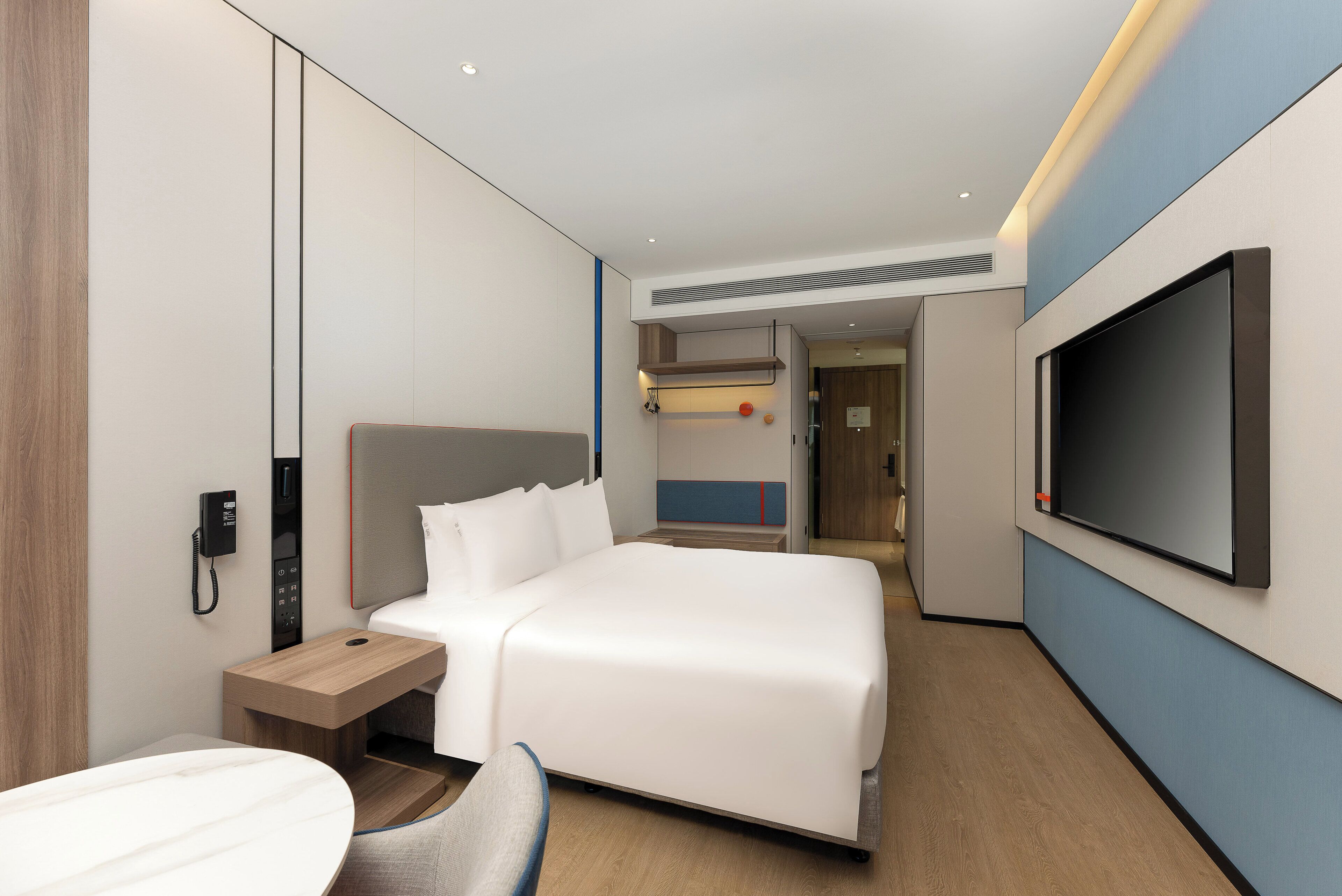 Een moderne hotelkamer met een groot bed, een nachtkastje, een aan de muur bevestigde televisie en een telefoon.