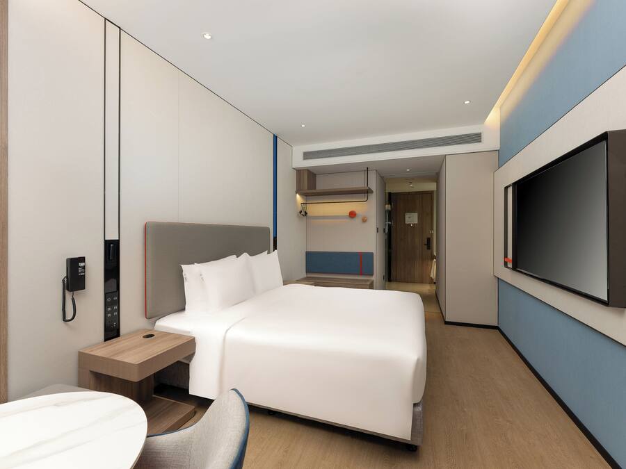 Een moderne hotelkamer met een groot bed, een nachtkastje, een aan de muur bevestigde televisie en een telefoon.