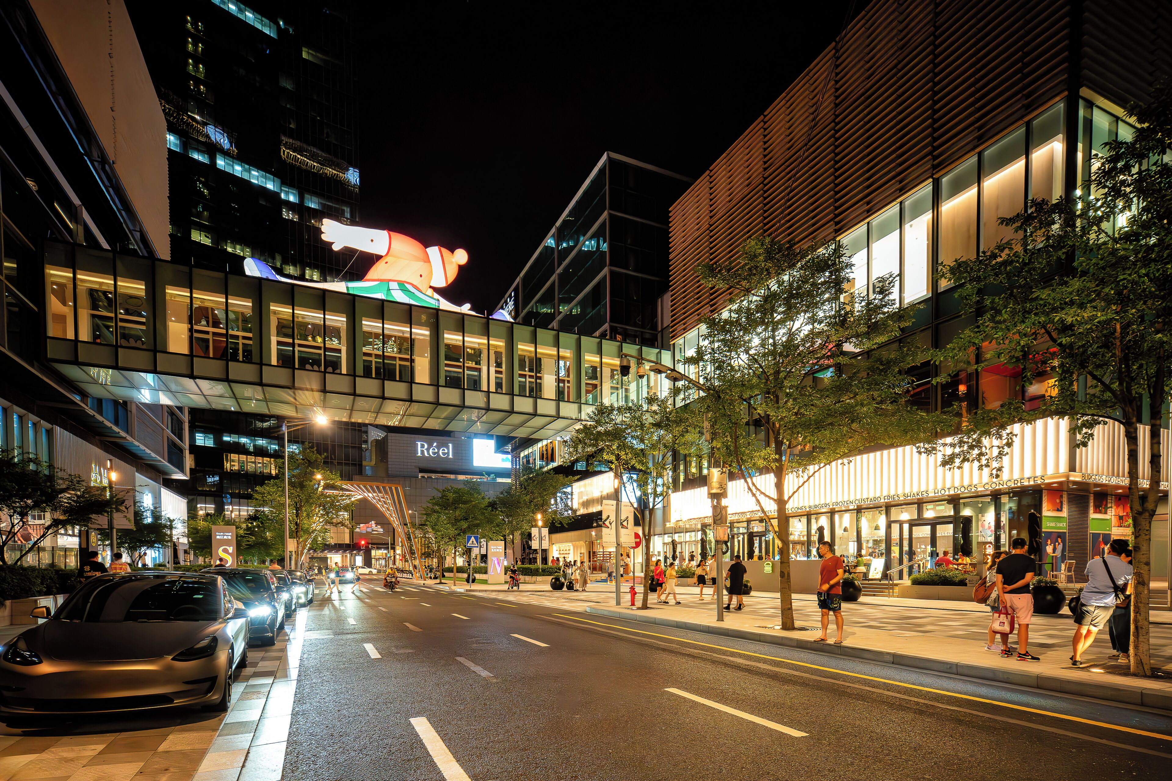 A modern urban street with a building featuring large windows and a sign that reads "Réal".