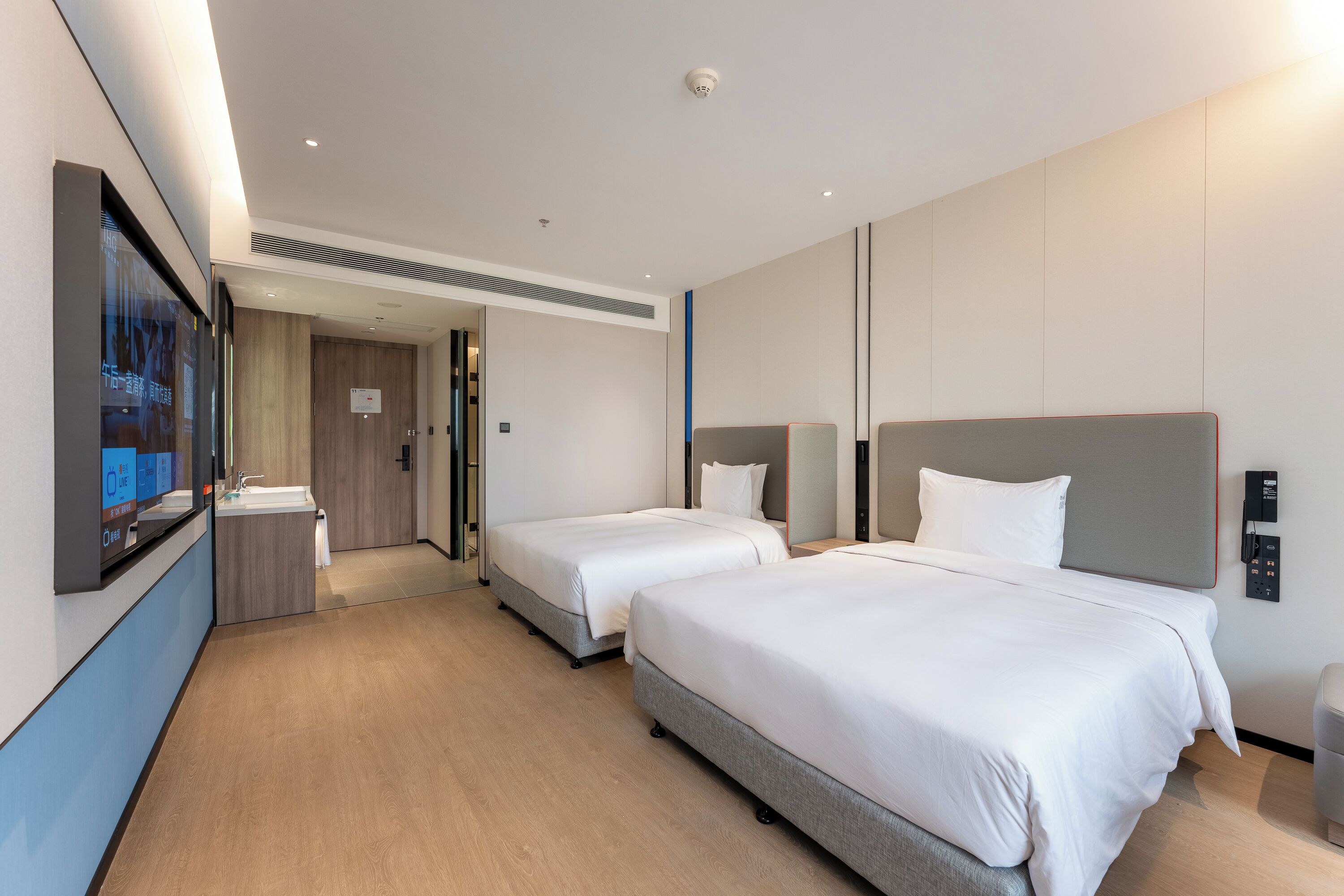 A hotel room with two beds, a large mirror, a sink, and a digital control panel.