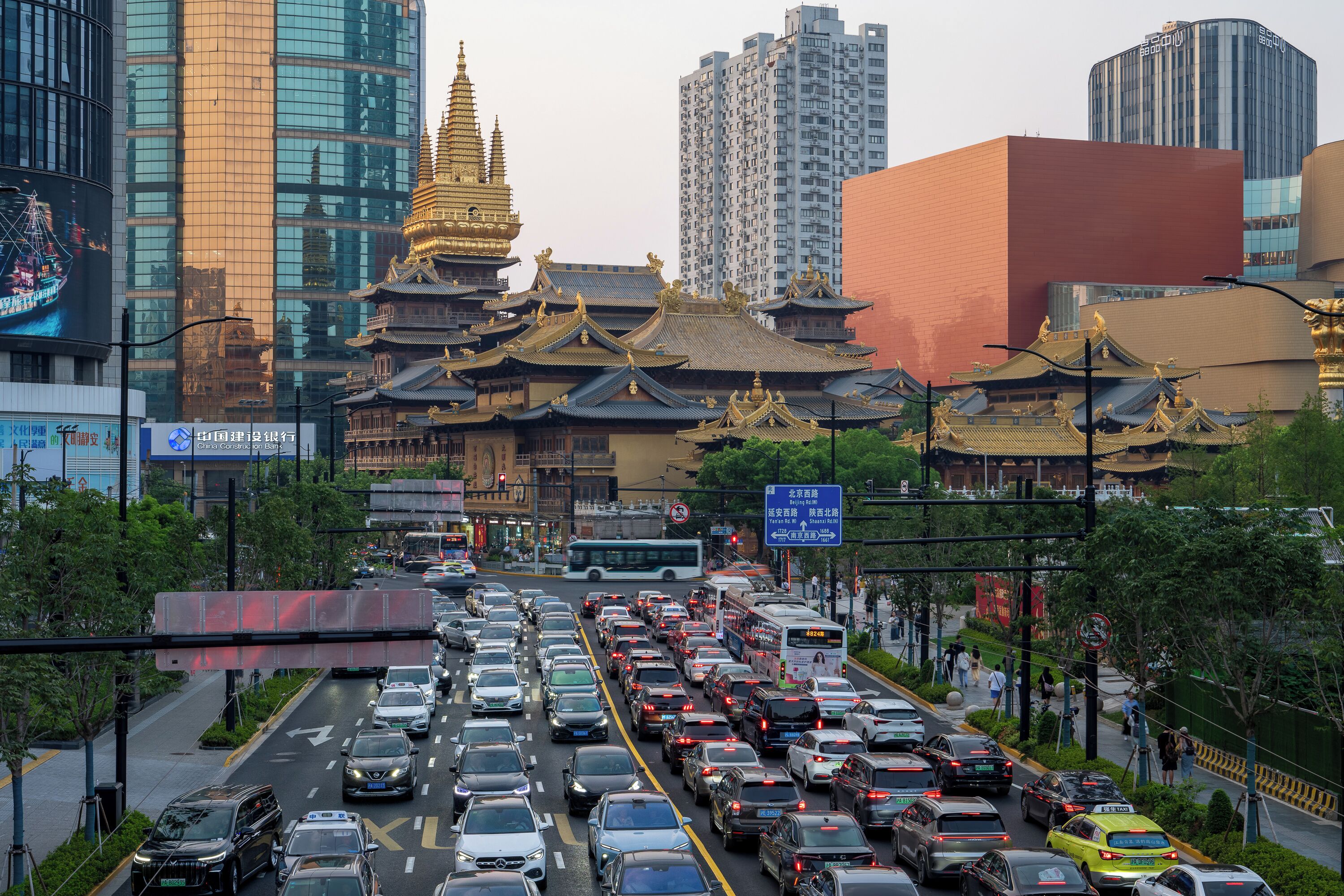 A busy urban street with traditional architecture in the background, including a golden pagoda and modern high-rise buildings.