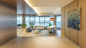 Ein modernes Wohnzimmer mit Sofa, Hocker und Couchtisch, ein Essbereich mit Stühlen und einem großen, abstrakten Kunstwerk an der Wand.