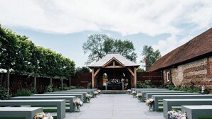 Een kapel met een houten dak en bakstenen muren, omringd door rijen banken met bloemdecoraties.