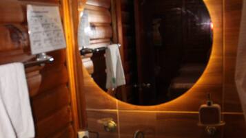 Un baño con paredes de madera, un espejo redondo, un lavabo y un perchero para toallas.