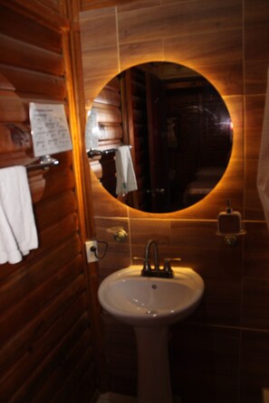 A bathroom with wooden walls, a round mirror, a sink, and a towel rack. - CABITAT CABAÑAS  (Quimbaya)