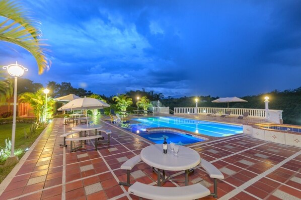 A swimming pool area with lounge chairs and umbrellas, surrounded by a tiled deck and palm trees.