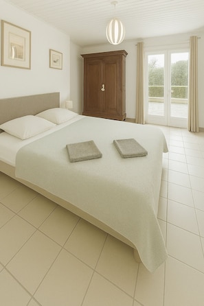 A bedroom with a large bed, a wooden wardrobe, and a view through a glass door.